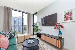 Ein modernes Wohnzimmer mit Sofa, Couchtisch, Fernseher, einer Topfpflanze und einem Blumenstrauß.