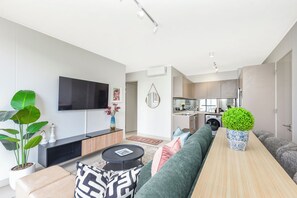 Ein modernes Wohnzimmer mit Sofa, Couchtisch, Fernseher und einer Küche im Hintergrund.