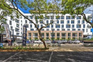 Ein modernes Gebäude mit mehreren Stockwerken, einem Parkplatz und einem Baum im Vordergrund.