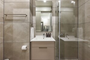 Une salle de bain moderne avec une douche à parois de verre, un lavabo blanc avec un miroir au-dessus et un porte-serviettes.