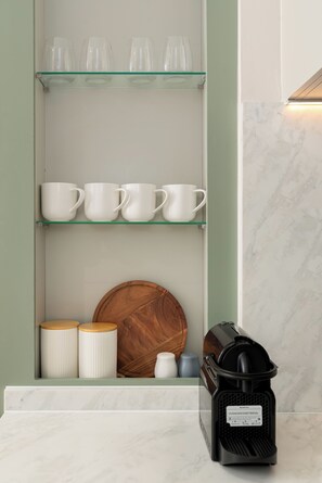A kitchen counter with a coffee maker, a wooden cutting board, and white mugs on a shelf. - Charlie and the Chairman | CBD Retreat | Balcony (Cape Town)