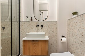 Un baño con un mueble de madera, un lavamanos blanco, un espejo y un inodoro.