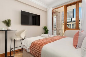 A hotel room with a bed, a TV mounted on the wall, a small table with a chair, and a window with a view of buildings. - Charlie and the Chairman | CBD Retreat | Balcony (Cape Town)