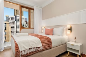 A hotel room with a bed, a nightstand, a window with a view of buildings, and a cityscape. - Charlie and the Chairman | CBD Retreat | Balcony (Cape Town)