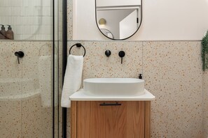A bathroom with a white sink, wooden cabinet, and a mirror above it. - Charlie and the Chairman | Contemporary Suite (Cape Town)