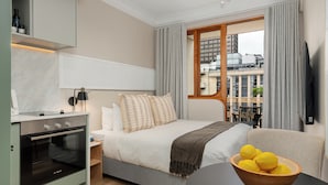 Ein modernes Hotelzimmer mit einem Bett, einem Holztisch mit Zitronen, einem Einbauofen und Blick auf die Stadt.