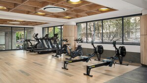 Ein Fitnessraum mit Trainingsgeräten, großen Fenstern und einer Holzbalkendecke.