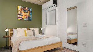 Een slaapkamer met een houten bed, een grote spiegel, een schilderij en een nachtkastje met een lamp.
