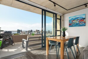 A balcony with a grill, a dining table with chairs, a painting on the wall, and a view of the cityscape. - Skyline Escape | Views, Pool and Braai (Cape Town)