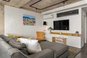 A modern living room with a grey sofa, a painting, a TV, and a plant. - Skyline Escape | Views, Pool and Braai (Cape Town)