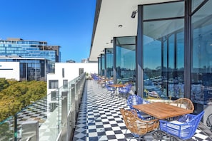 Eine Dachterrasse mit Schachbrettböden, Glasgeländern und Sitzmöbeln im Freien.