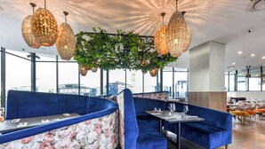 Moderni ravintola, jossa on siniset samettiset istuinalueet, kukkakuviolliset sermit ja katosta roikkuvat valaisimet.