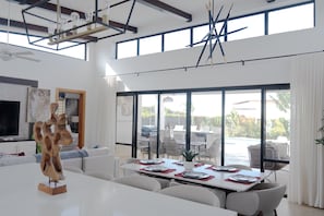 A spacious living area with a dining table set for four, large windows, and a modern ceiling design. - Tan Villas & Country Club (Sosúa)