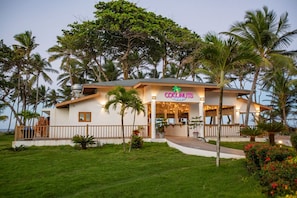 Ein zweistöckiges Gebäude mit einem Schild, auf dem 'Coconuts' steht, und Blick auf den Strand.