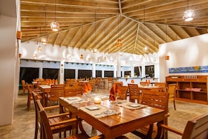 A spacious dining area with wooden tables and chairs, pendant lighting, and a high ceiling. - Tan Villas & Country Club (Sosúa)