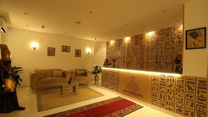 Una sala de estar con sofá, mesa de centro y alfombra roja. Hay decoraciones en las paredes, incluyendo jeroglíficos y una fotografía enmarcada.