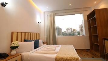 Quarto de hotel com cama, mesa de cabeceira, armário de madeira e janela com cortinas.