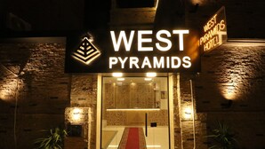 El exterior del Hotel West Pyramids, con un cartel llamativo, una alfombra roja que conduce a la entrada y paredes de piedra.
