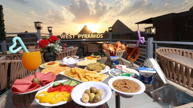 Una mesa servida con comida y bebidas, vista a las Pirámides de Giza y una puesta de sol.