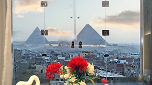 Vista de las pirámides a través de una ventana, un florero con flores y dos jarrones sobre una mesa.