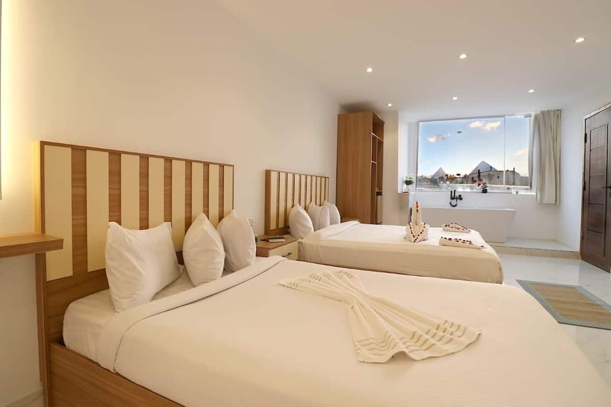 Habitación de hotel con dos camas, un ventanal con vistas a una pirámide, una bañera y un armario.