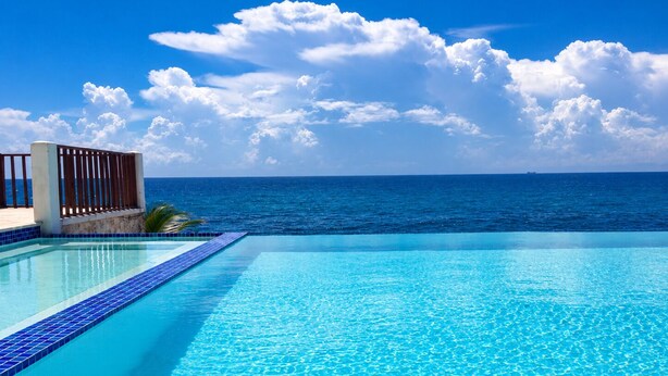 Una piscina infinita de color azul cristalino con una cubierta de madera y vista al océano.