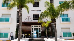 Un edificio con un letrero que dice 'Costa Cabey Juan dolio', con un diseño moderno que incluye listones horizontales de madera, una entrada de vidrio y palmeras.