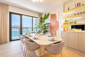 A dining area with a large table set for six, surrounded by wicker chairs, a potted plant, and a view of the city through large windows. - New Spacious Family 3BR + Kids Room with Sea View (Dubai)