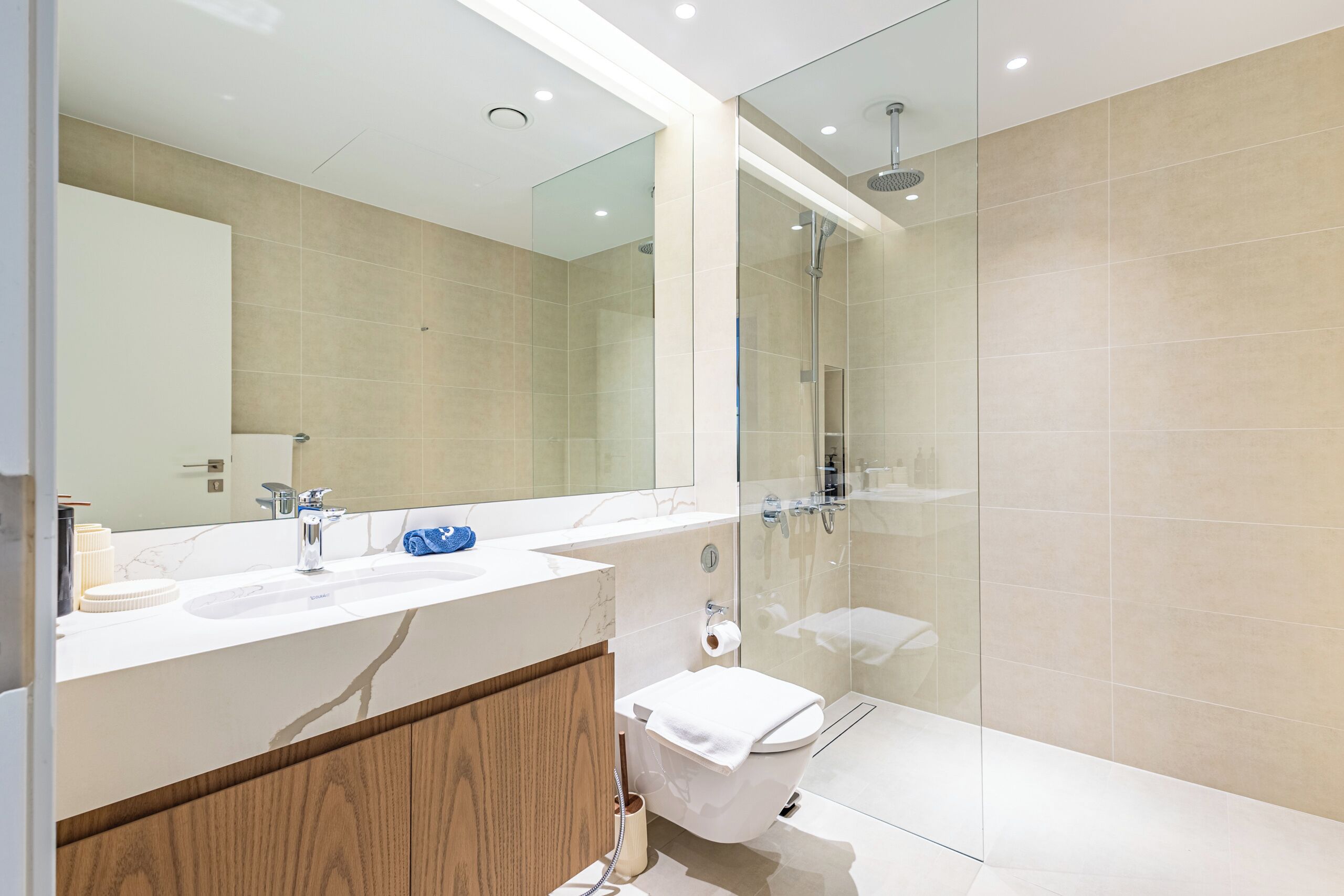 Ett modernt badrum med en duschkabin i glas, en vit tvättställ och ett badrumsskåp i trä.