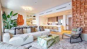 Un salon moderne avec un canapé, une table basse et un fauteuil. On aperçoit un coin cuisine au fond.