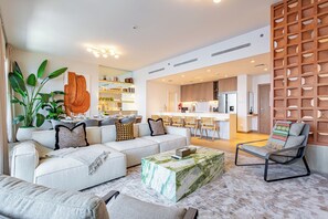 Ein modernes Wohnzimmer mit einer Couch, einem Couchtisch und einem Sessel. Im Hintergrund befindet sich eine Küchenzeile.