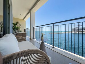 Ein Balkon mit Meerblick, eine Couch, ein Tisch mit einer Vase und eine Topfpflanze.
