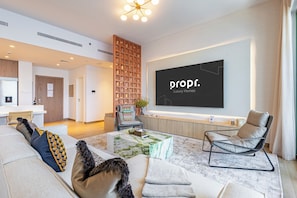 Uma sala de estar moderna com uma televisão de tela plana grande, um sofá, uma mesa de centro e uma poltrona.