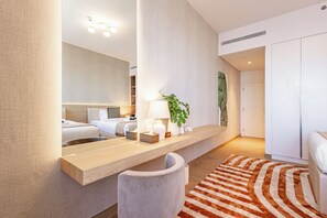 Ein Hotelzimmer mit einem großen Spiegel, einem Nachttisch mit Lampe, einer Zimmerpflanze, einem Streifen Teppich und einem Kleiderschrank.