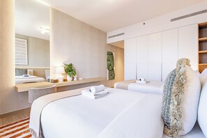 Una habitación de hotel con una cama grande, una mesita de noche con lámpara, un espejo, una planta y un armario.