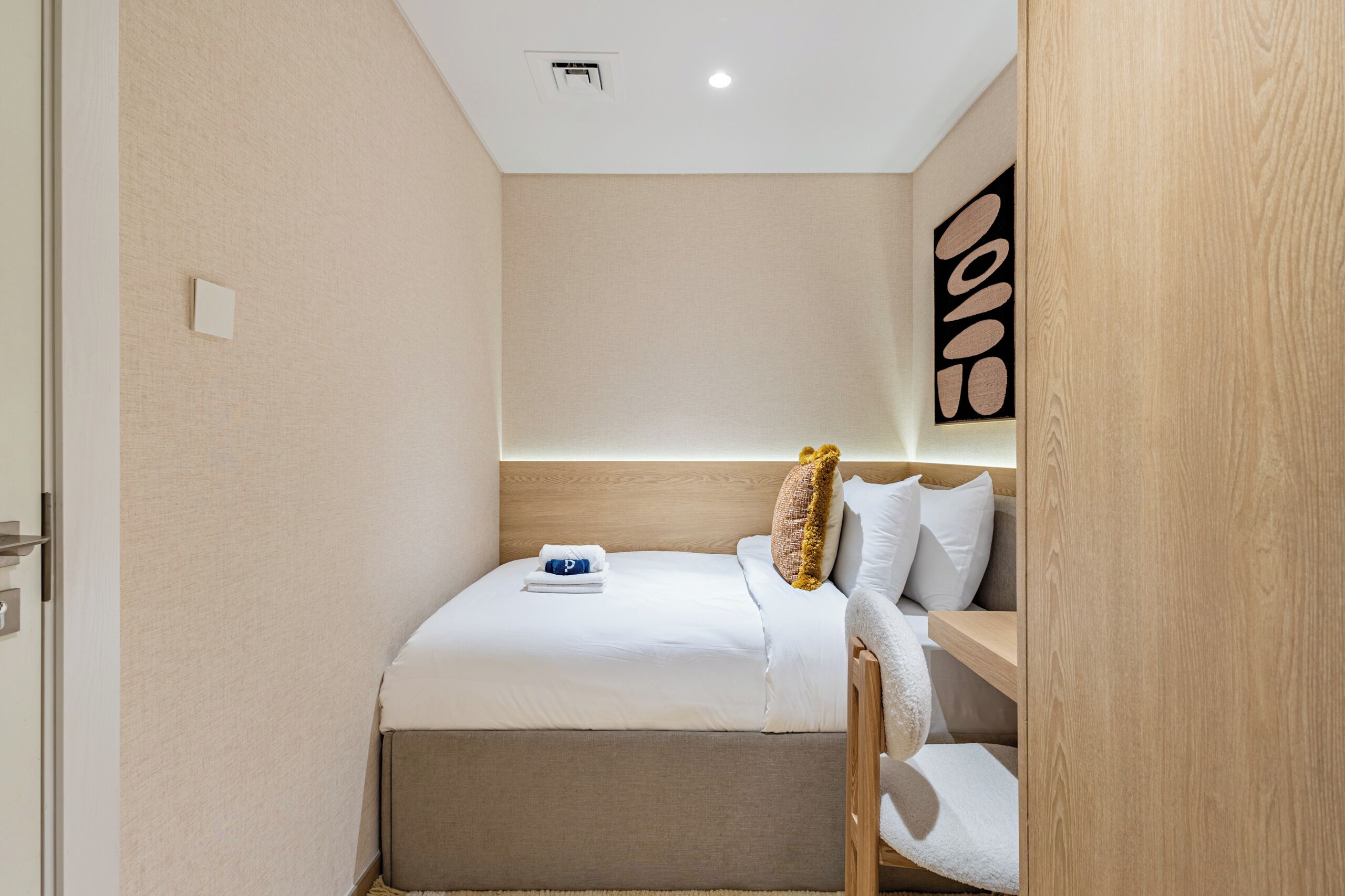 Ein kleines Hotelzimmer mit einem Bett, einem Holzkopfteil, einem Wandbild und einem kleinen Regal.