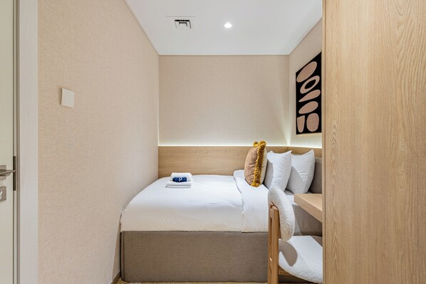 Quarto de hotel pequeno com uma cama, cabeceira de madeira, uma obra de arte pendurada na parede e uma pequena prateleira.