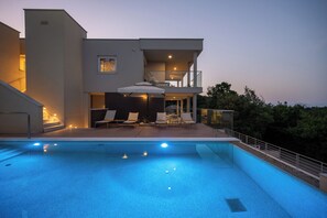 Et moderne hus med swimmingpool, udendørs møbler og en balkon.
