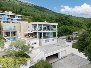 En moderne boligbygning med flere etager, swimmingpool, altaner og udsigt til en grøn bakke.