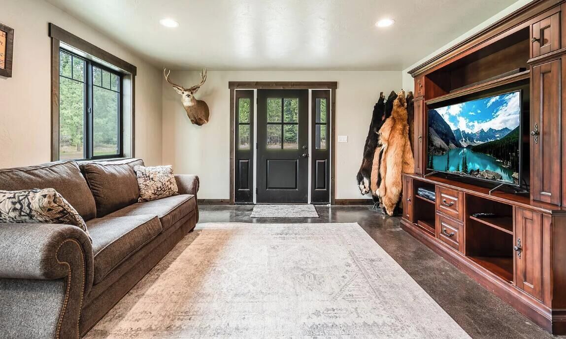 A living room with a sofa, a television, a rug, and mounted animal heads.