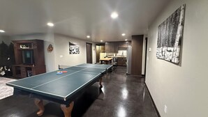 Una habitación con mesa de ping pong, zona de cocina y mesa de comedor con sillas.