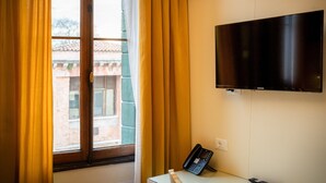 Ein Zimmer mit Fenster, Vorhängen, einem Flachbildfernseher, einem Schreibtisch mit Telefon und einer Wandsteckdose.