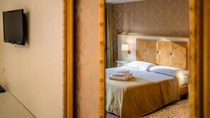 Ein Hotelzimmer mit einem Bett, einem an der Wand montierten Fernseher und einem Spiegel, der einen Teil des Raumes reflektiert.