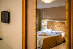 Quarto de hotel com uma cama, televisão na parede e um espelho refletindo parte do espaço.