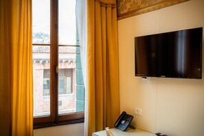 Ein Zimmer mit Fenster, Vorhängen, einem Flachbildfernseher, einem Schreibtisch mit Telefon und einer Wandsteckdose.