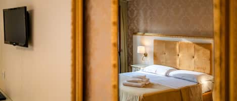 Una habitación de hotel con una cama, un televisor en la pared y un espejo que refleja parte del cuarto.