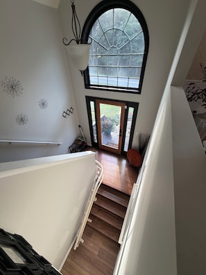 A staircase leading to a second-floor landing with a large arched window, a white wall with decorative elements, and a wooden floor. - Cozy 1-bedroom in a spacious house with AC in charming Powder Springs (Powder Springs)