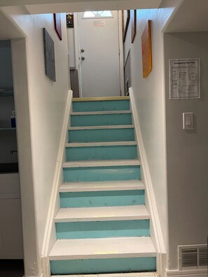 A staircase with teal steps and white handrails, leading to a door with a sign above it.
