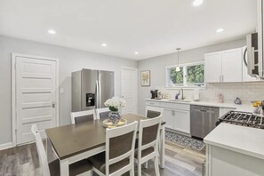 A modern kitchen with white cabinetry, a stainless steel refrigerator, a dining table with chairs, and a window providing natural light. - Spacious 4-bedroom house - St. Charles with AC (St. Charles)