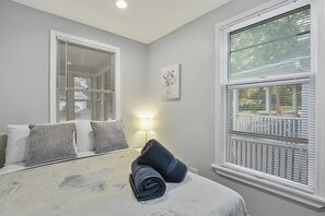 A bedroom with a bed, pillows, a bedside lamp, and a window with blinds. - Spacious 4-bedroom house - St. Charles with AC (St. Charles)